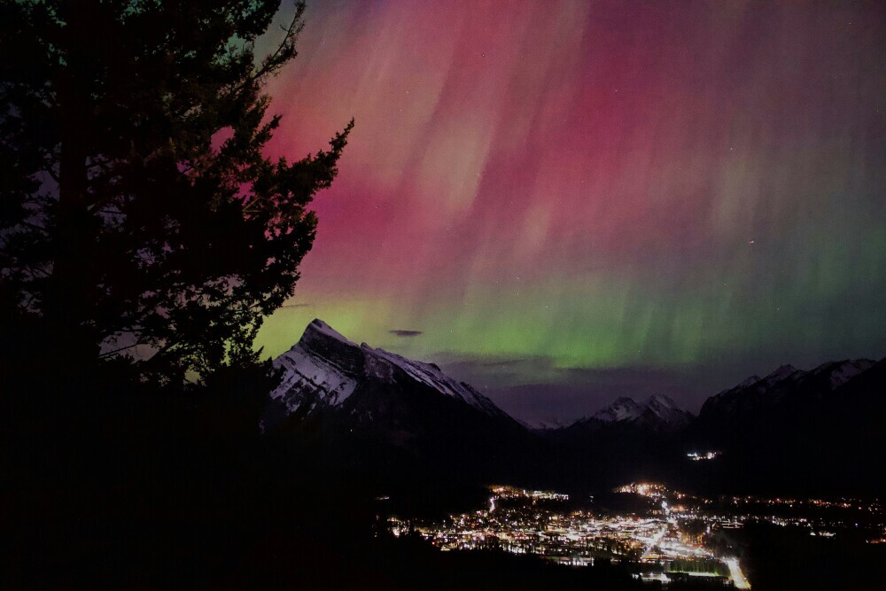 A long-exposure photograph of the Northern Lights, with streaks of purple, pink, and green light illuminating the night sky. The colors blend smoothly, creating a soft, ethereal effect against the dark backdrop dotted with faint stars. The image captures the beauty and tranquility of the aurora borealis as it flows across the sky in gentle, sweeping motions.