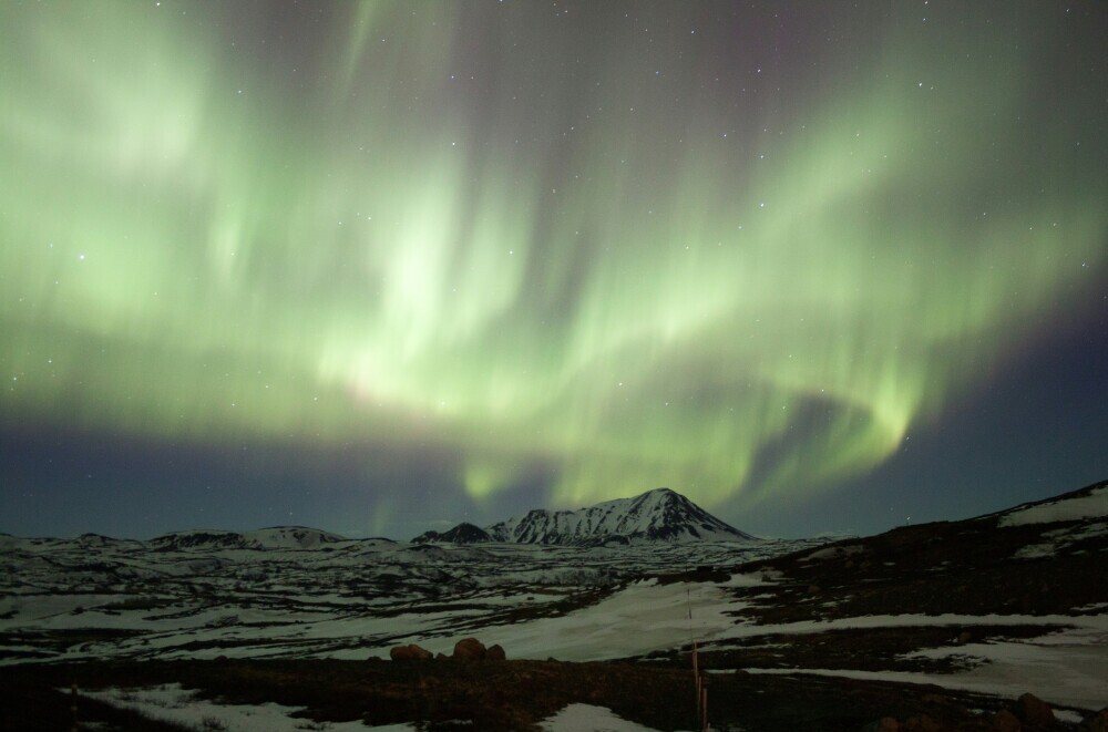 Stunning green Northern Lights dancing above a snow-covered mountain landscape under a starry sky.